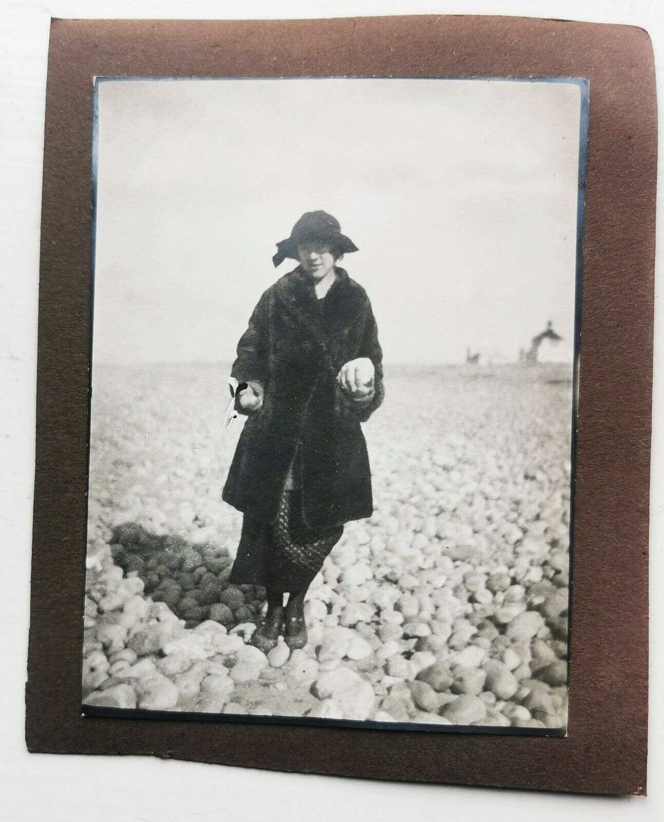 Old photo: Woman with hat and coat on stone field with stone in her hand  Fo584