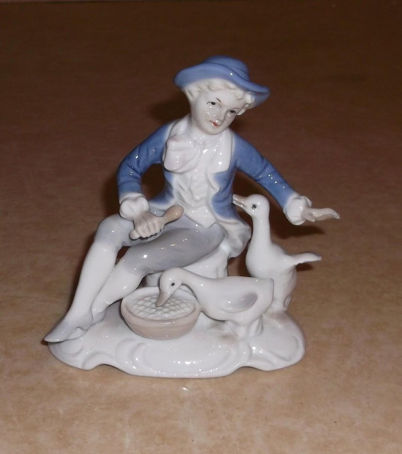 Figurin pojke med blå kläder som matar två vita gäss porslin