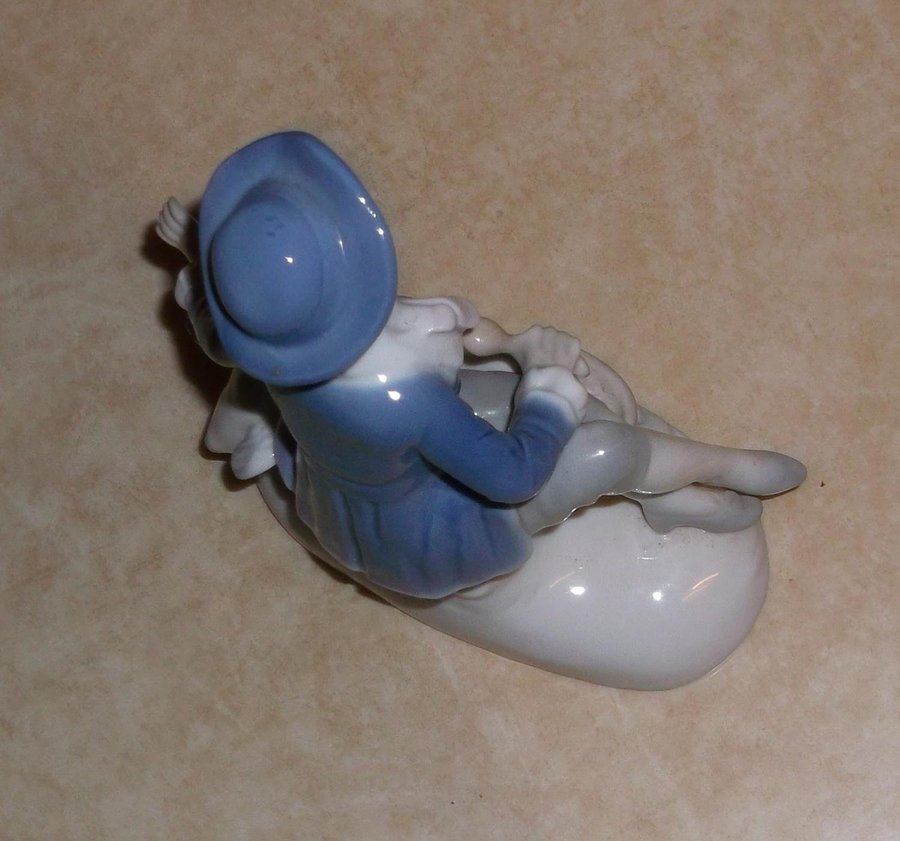 Figurin pojke med blå kläder som matar två vita gäss porslin
