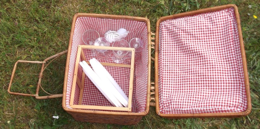 Picknick korg av rotting vit och röd rutigt tyg på insidan med innehåll